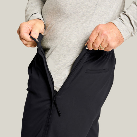 Man in a gray shirt pulling open the waist-to-ankle side zipper of black pants at the hip