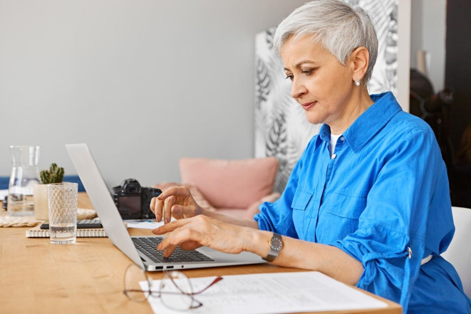 Older woman sitting at a desk working on a laptop. Cover art for AskSAMIE blog titled How to launch a thriving enterprise that supports caregivers