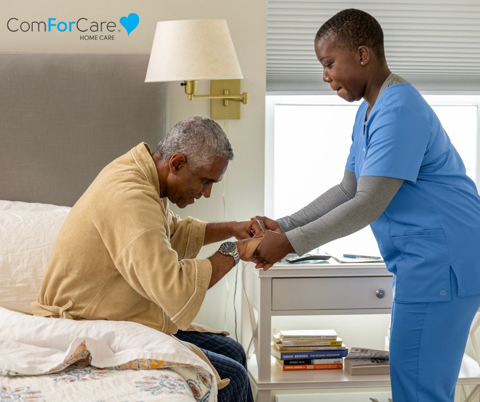 ComForCare | In Home Care Service woman in scrub helping an elderly man to stand from bed by AskSAMIE