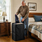 Older man drops a shirt into the laundry backpack standing upright as a bedroom hamper, his walking cane resting by the nightstand.