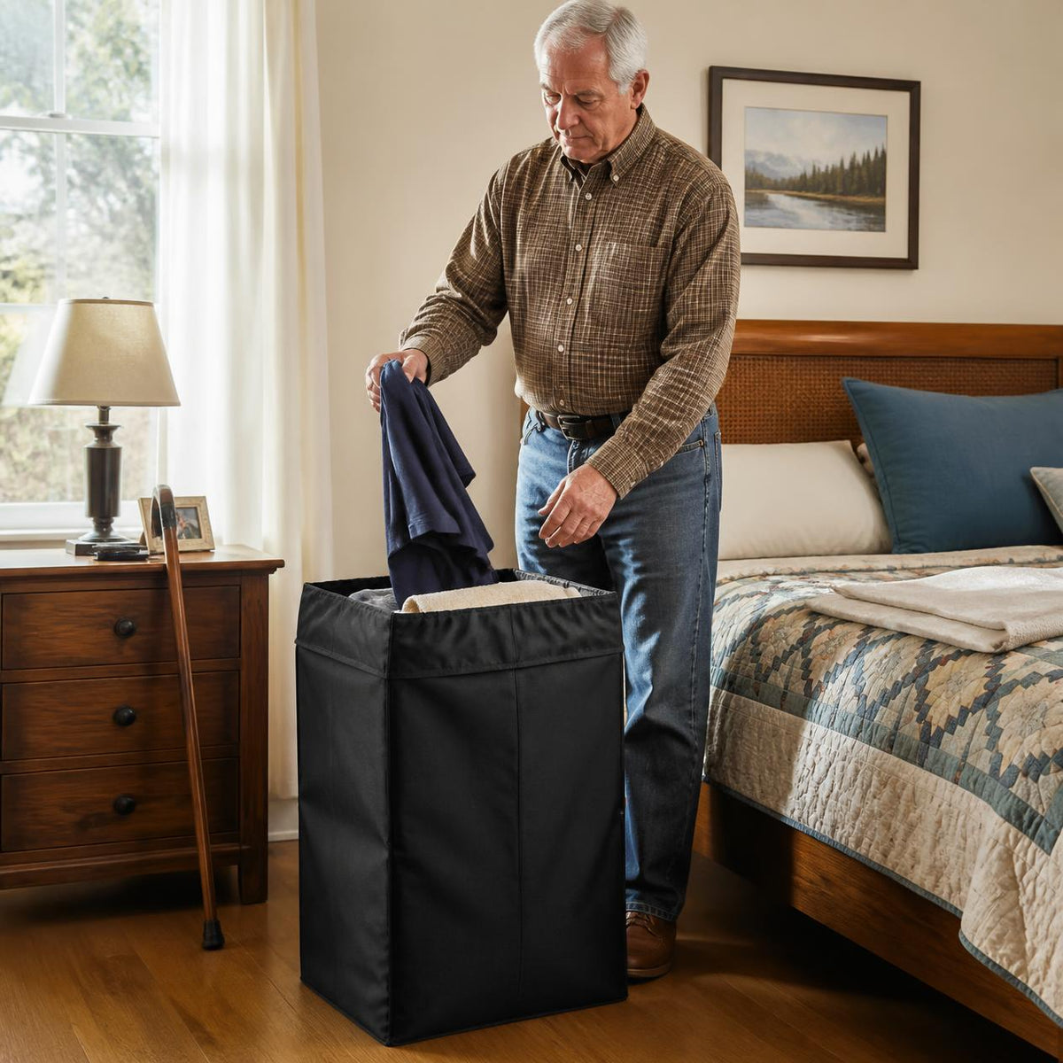 Older man drops a shirt into the laundry backpack standing upright as a bedroom hamper, his walking cane resting by the nightstand.