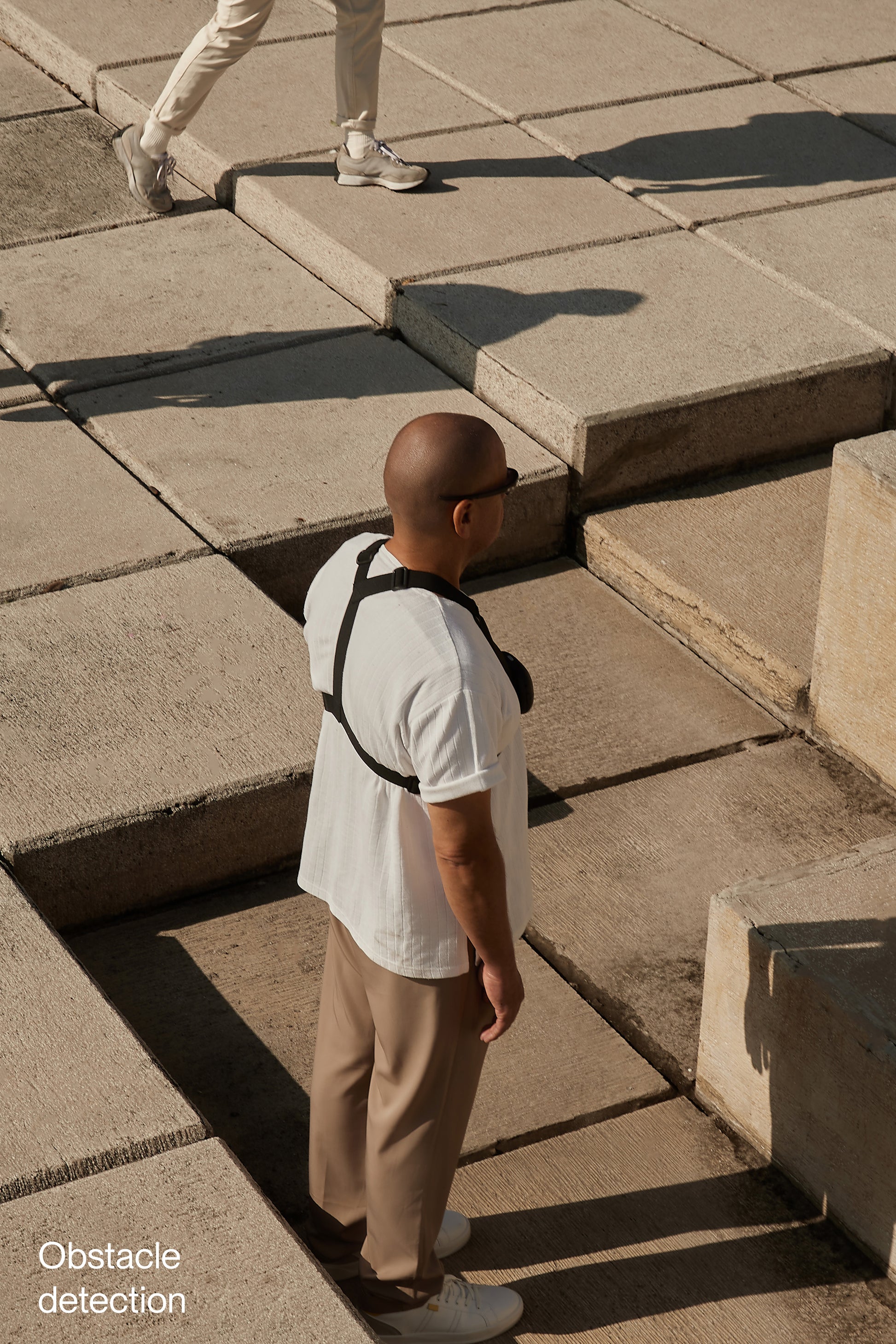 Man shown standing outside with concrete block in front of him, he has glasses and Are device strapped to his upper body.