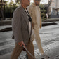 The image shows 2 men walking across a cross walk, one with glasses,  Ara and a white cane. The other man is walking along side him.