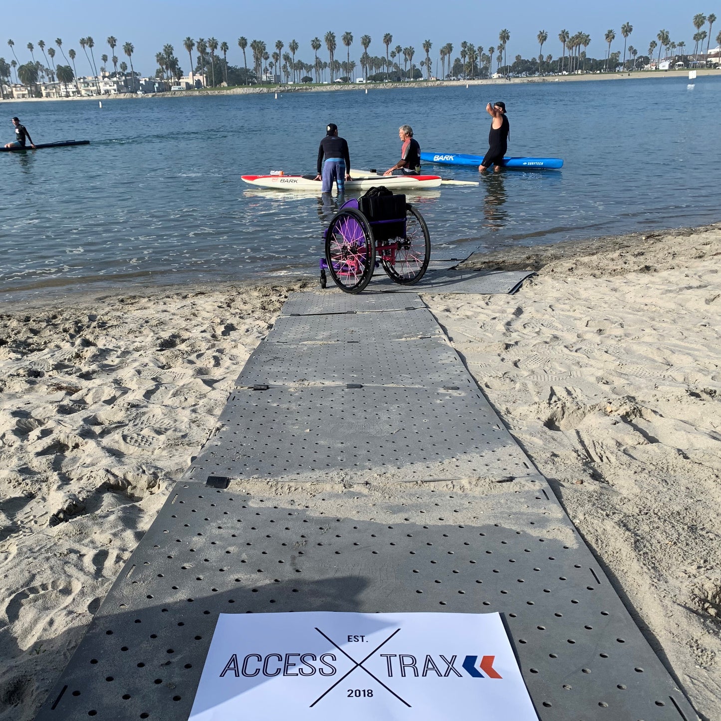 AccessTrax being used on the beach with canoes in the lake and a manual wheelchair at the end of the AccessTrax