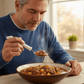 Man in a blue sweater lifts a spoonful of steaming beef stew with the white-handled swivel spoon, its bowl staying level