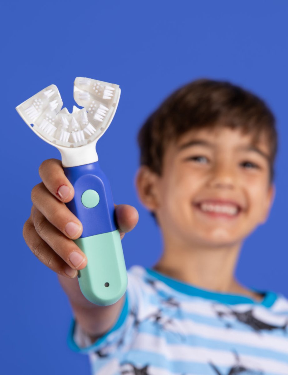 A smiling boy holding out the SymplBrush Jr. adaptive toothbrush for kids ages 5 to 12.