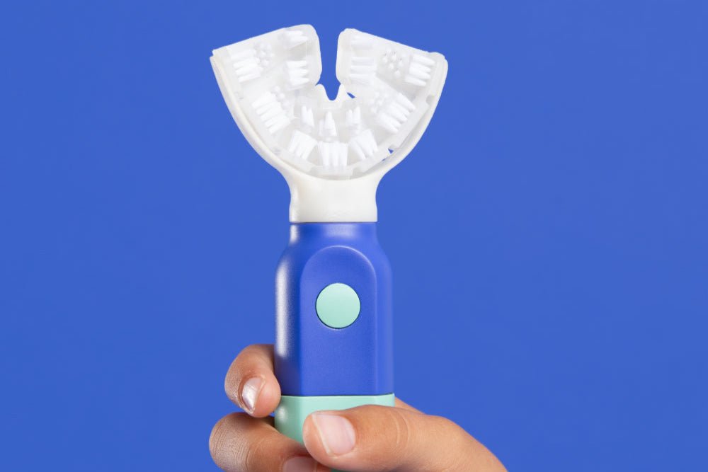 A child's hand holding the Blue and Aqua SymplBrush Jr. by its wide barrel handle, which needs no fine motor control to grip.