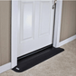 Close up of a black rubber threshold ramp butted against the sill of a white entry door, forming one continuous slope from the concrete up over the threshold.